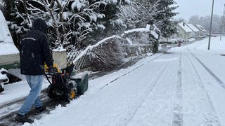 Erster Schnee im Allgäu am Wochenende, Mann fräst mit Schneefräse den Weg frei