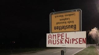 Umgedrehtes Ortsschild von Baustetten und Pappschild mit Text "Ampel ausknipsen"