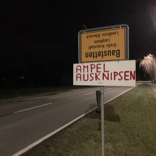 Umgedrehtes Ortsschild von Baustetten und Pappschild mit Text "Ampel ausknipsen"