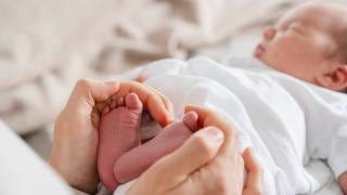 Frauenhände umschließen die Füße eines neugeborenen Babys. 