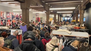 Besucher des Kostuemverkaufs des Theater Konstanz stöbern in den Sachen und zeigen ihre Fundstücke wie ein gestreiftes Jacket oder einen übergroßen Mantel aus dem Weihnachtsmärchen