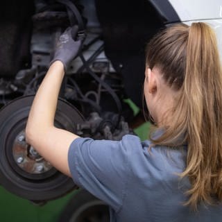 Eine KFZ-Mechanikerin wechselt in einer KFZ-Werkstatt die Bremsscheibe eines Autos.