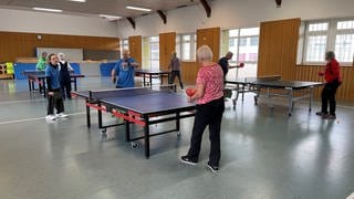 Parkinson-Patienten spielen in einer Turnhalle zu zweit oder zu dritt Tischtennis