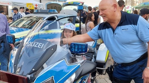 Ein Kind sitzt auf einem Polizeimotorrad auf der Blaulichtmeile auf dem Biberacher Marktplatz. Ein Polizist zeigt etwas am Motorrad. Die Heimattage in Biberach haben mit einem ersten Festwochenende begonnen.