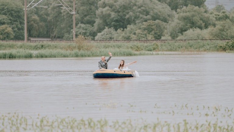 Das Brautpaar sitzt für Hochzeitsfotos im Schlauchboot und paddelt über ein überflutetes Feld