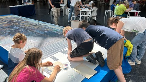 Die Messebesucher puzzeln am 32.000-Teile-Puzzle auf der Spielemesse in Friedrichshafen