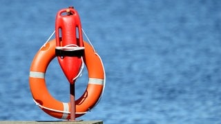 Ein Rettungsring und eine Rettungsboje hängen am Rand einer Wasseroberfläche. 