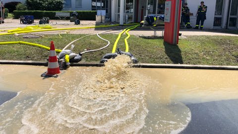 Brauenes Wasser spritzt in einer Fontäne aus gelben Schläuchen, die aus einer Bankfiliale zur Straße ausgelegt sind. Die Feuerwehr pumpt die Filiale der Sparkasse in Oberteuringen aus. 