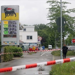 Ein Bereich nahe einer Tankstelle ist mit Absperrband gesichert, im Hintergrund ist ein Polizeiwagen zu sehen.