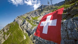 Eine große Schweizer Flagge wird am Säntis entrollt und hängt am Nationalfeiertag am Felsen.
