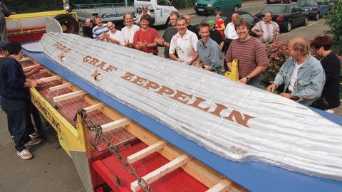 Helfer heben einen riesigen Zeppelin aus Biskuit auf einen Transporter 