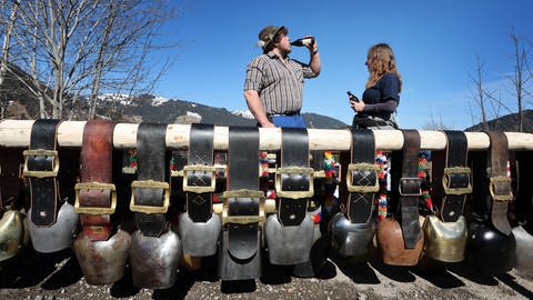 Teilnehmer des Weltrekordversuchs im Kuhschellenläuten stehen in Bad Hindelang hinter Kuhschellen.