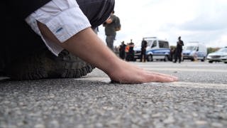 Ein Klimaaktivist klebt mit seiner Hand auf dem Asphalt