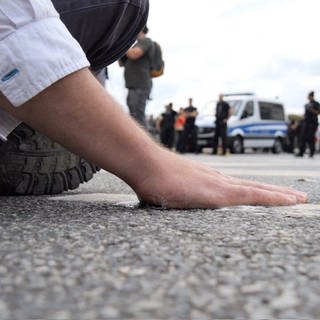 Ein Klimaaktivist klebt mit seiner Hand auf dem Asphalt