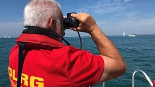 Ein Retter der DLRG beobachtet den Bodensee durch sein Fernglas.