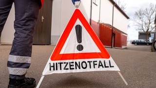 Notarzt stellt ein Warndreieck auf, auf dem "Hitzewarnung" steht.