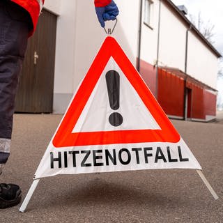 Notarzt stellt ein Warndreieck auf, auf dem "Hitzewarnung" steht.