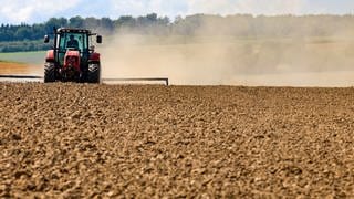 Ein Landwirt bearbeitet ein abgeerntetes Feld und wirbelt dadurch eine Staubwolke auf