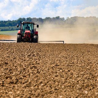 Ein Landwirt bearbeitet ein abgeerntetes Feld und wirbelt dadurch eine Staubwolke auf