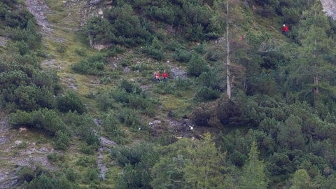 Einsatzkräfte an steilem Berghang und einzelne Wrackteile