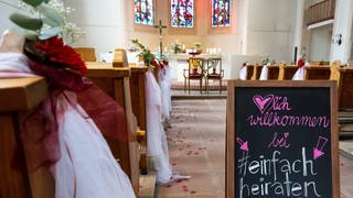 Ein Schild in einer geschmückten Kirche: Herzlich willkommen bei "einfach heiraten"