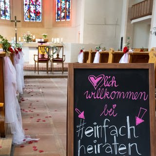 Ein Schild in einer geschmückten Kirche: Herzlich willkommen bei "einfach heiraten"