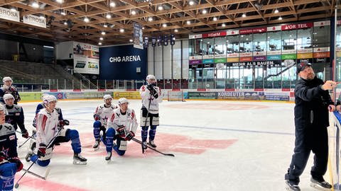 Der neue Trainer erklärt den Towerstars Spieler auf dem Eis einen Spielzug an einer Tafel.