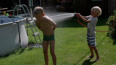 Oscar spritzt seinen Bruder Peter mit einem Wasserschlauch nass.