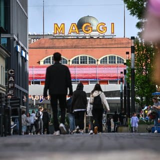 Der Schriftzug MAGGI ist auf einem historischen Gebäude des Unternehmens Maggi angebracht, während im Vordergrund Menschen durch die Innenstadt laufen. 