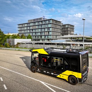 Schwarz-gelber Kleinbus fährt auf einer Straße vor einem ZF-Bürogebäude