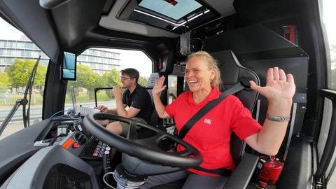 Eine Busfahrerin sitzt am Steuer mit erhobenen Händen