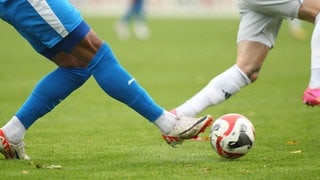 Beine von Fußballspielern auf einem Fußballplatz mit Ball