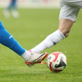 Beine von Fußballspielern auf einem Fußballplatz mit Ball