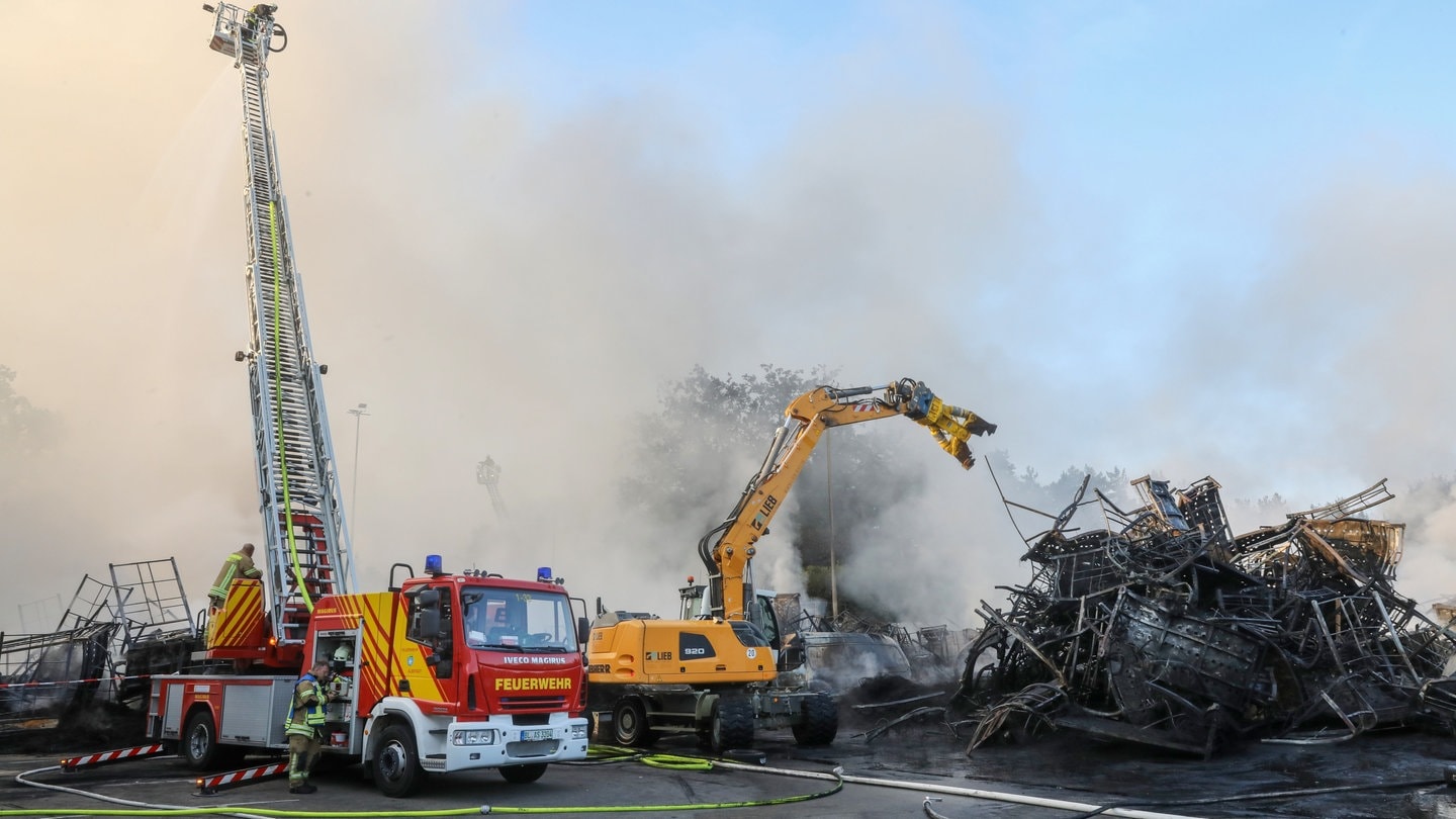 Einsatzkräfte der Feuerwehr stehen während eines Großbrandes auf dem Gelände eines Reifengroßhändlers und löschen das Feuer.