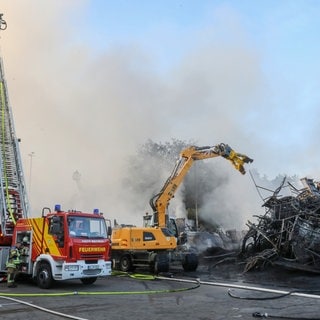 Einsatzkräfte der Feuerwehr stehen während eines Großbrandes auf dem Gelände eines Reifengroßhändlers und löschen das Feuer. 