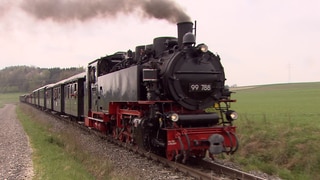 Eine historische Schmalspurbahn fährt durch die Landschaft