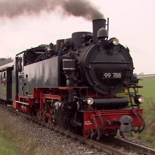 Eine historische Schmalspurbahn fährt durch die Landschaft