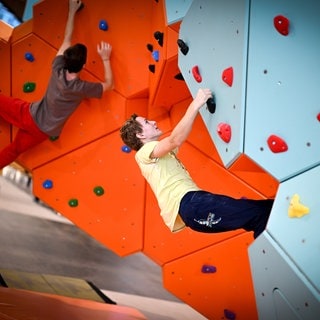 Zwei junge Männer hängen in einer Kletterwand. Ums Klettern geht es bei der Messe Vertical Pro in Friedrichshafen.