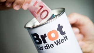 Ein Zehn-Euro-Geldschein wird in eine Spendendose von "Brot für die Welt" geschoben.