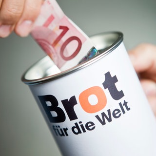 Ein Zehn-Euro-Geldschein wird in eine Spendendose von "Brot für die Welt" geschoben.