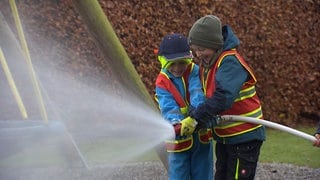 Zwei Jungs halten einen Feuerwehrschlauch aus dem Wasser spritzt.