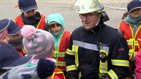 Ein Mann hat sich auf den Boden gekniet, um Kindern etwas zu erklären.