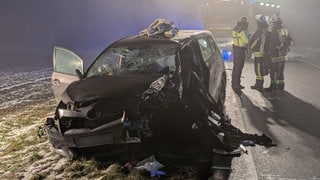 Nach einem Frontalzusammenstoß auf der Bundesstraße 30 in Bad Waldsee (Kreis Ravensburg) stehen Rettungskräfte vor einem zerstörten Auto.