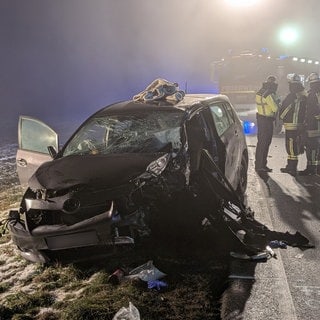 Nach einem Frontalzusammenstoß auf der Bundesstraße 30 in Bad Waldsee (Kreis Ravensburg) stehen Rettungskräfte vor einem zerstörten Auto.