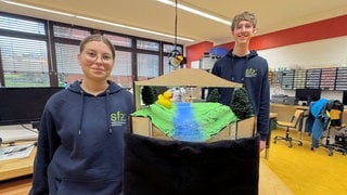 Jana und Niklas stehen am Modell ihres Hochwasser-Warnsystems