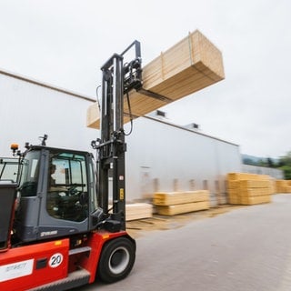 Ein Gabelstapler transportiert zugesägtes Holz über das Gelände eines Sägewerks. 