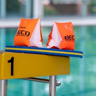 Zwei Schwimmflügel und ein Schwimmbrett liegen auf einem Startblock in einer Schwimmhalle.