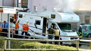 Feuerwehrleute und Polizisten stehen am 04.11.2011 in Eisenach (Thüringen) vor einem qualmenden Wohnmobil, in dem zwei Leichen entdeckt wurden. In dem Fahrzeug hatten sich die beiden Männer der Neonazi-Terrorzelle (NSU) umgebracht. 