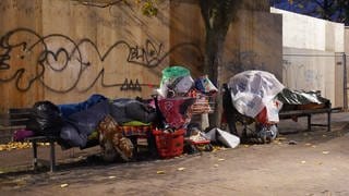 Zwei obdachlose Mesnchen schlafen umgeben von ihrem Hab und Gut auf Bänken unter einer Brücke