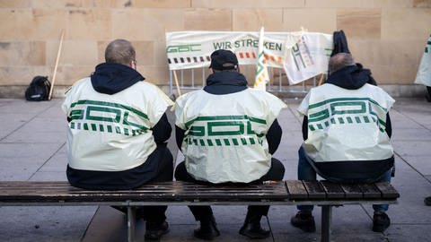 Teilnehmer eines Warnstreiks der Gewerkschaft Deutscher Lokomotivführer (GDL) sitzen vor dem Heilbronner Hauptbahnhof auf einer Bank